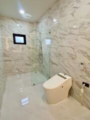 Modern bathroom with marble walls and floors, glass shower enclosure, and smart toilet