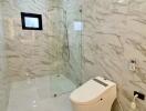 Modern bathroom with marble walls and floors, glass shower enclosure, and smart toilet