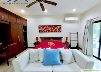 Modern bedroom with red bedding and a sofa, featuring a ceiling fan and sliding glass door.