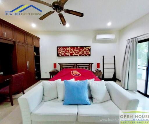 Modern bedroom with red bedding and a sofa, featuring a ceiling fan and sliding glass door.