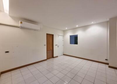 Spacious empty living room with white tiles, wooden accents, window, and air conditioning unit