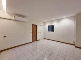 Spacious empty living room with white tiles, wooden accents, window, and air conditioning unit