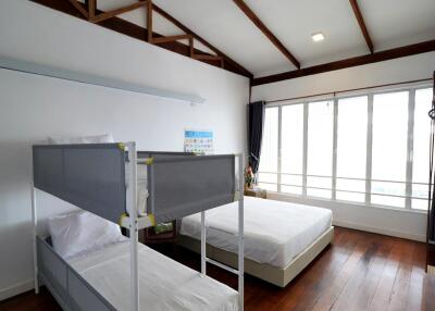 Bedroom with high ceiling, two beds, large window, and wooden floor