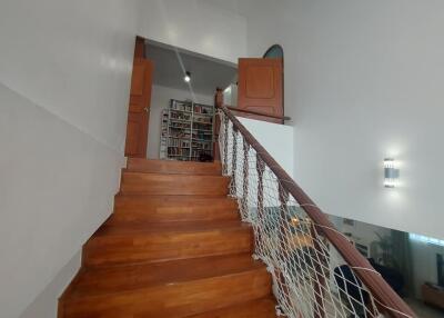 Interior wooden staircase with net railing leading to upper floor with view of bookshelves