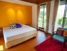 Cozy bedroom with a large bed, colorful pillows, wooden flooring, and large windows with curtains