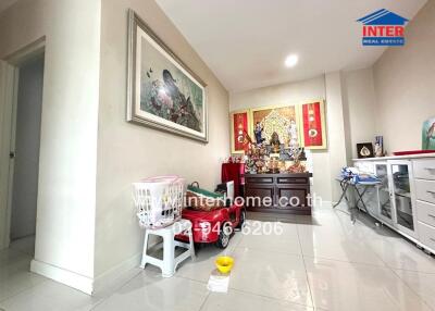 Living room with white tiled flooring, a cabinet with religious items, and a framed picture on the wall