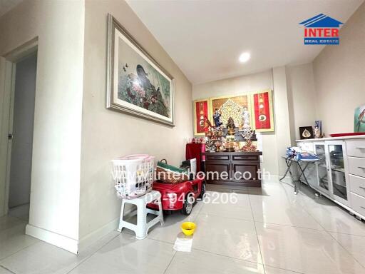 Living room with white tiled flooring, a cabinet with religious items, and a framed picture on the wall