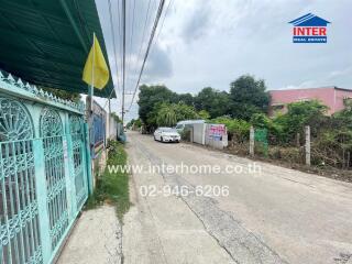 Residential street view with a gate, flag, and contact information