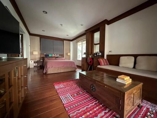 Spacious bedroom with a bed, sofa, wooden furniture, and a red patterned rug