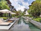 Outdoor swimming pool area with lounge chairs and umbrellas in a residential complex.