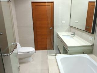 Modern bathroom with wooden door, toilet, sink, and bathtub