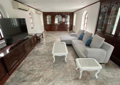 Spacious living room with a large TV, grey sectional sofa, and light-colored coffee tables