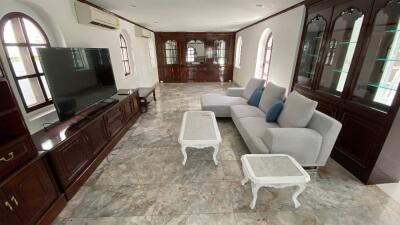 Spacious living room with a large TV, grey sectional sofa, and light-colored coffee tables