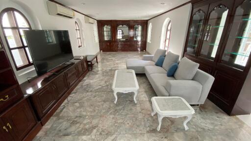 Spacious living room with a large TV, grey sectional sofa, and light-colored coffee tables