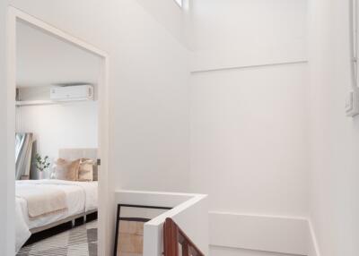 Brightly lit hallway with wooden staircase and view into a bedroom