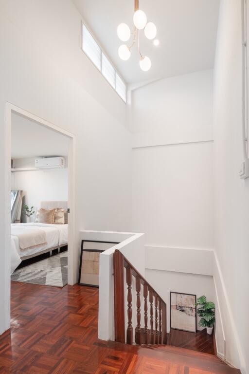 Brightly lit hallway with wooden staircase and view into a bedroom