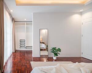 Spacious bedroom with wooden flooring, large window, minimalistic decor, and walk-in closet