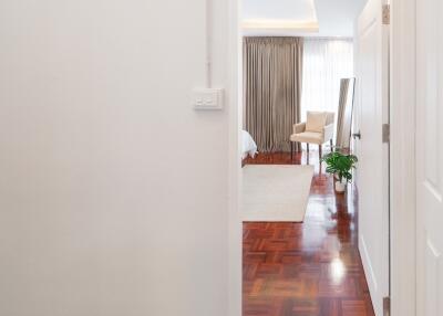 View through a hallway into a well-lit bedroom with wooden flooring.