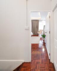 View through a hallway into a well-lit bedroom with wooden flooring.