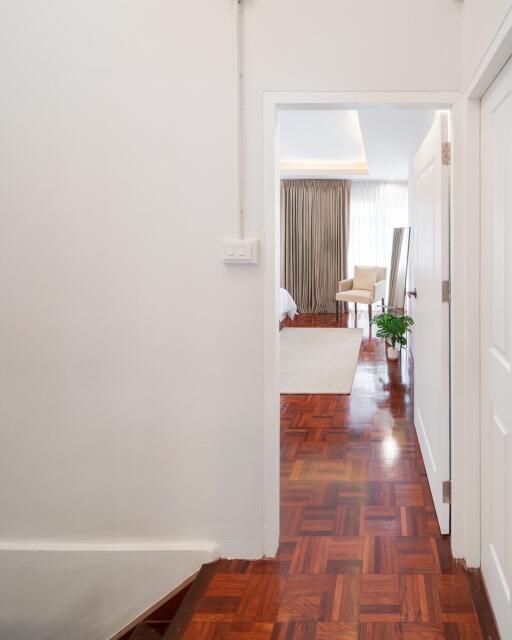 View through a hallway into a well-lit bedroom with wooden flooring.