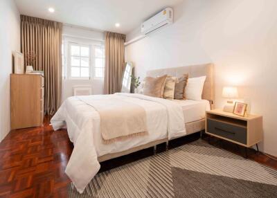 Modern bedroom with wooden floor, queen-sized bed, nightstand, dresser, window, and air conditioning unit