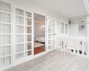 Balcony with white chairs and French doors leading into a bedroom