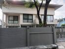 Exterior view of a two-story house with a front gate and trees