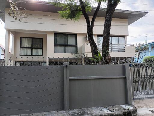 Exterior view of a two-story house with a front gate and trees