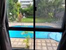 View of a swimming pool from a window with surrounding greenery