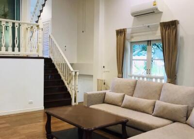 Living room with staircase, beige sofa, wooden coffee table, ceiling fan, and window with drapes