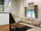 Living room with staircase, beige sofa, wooden coffee table, ceiling fan, and window with drapes