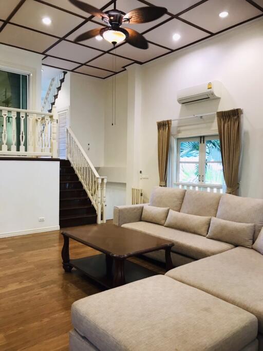 Living room with staircase, beige sofa, wooden coffee table, ceiling fan, and window with drapes