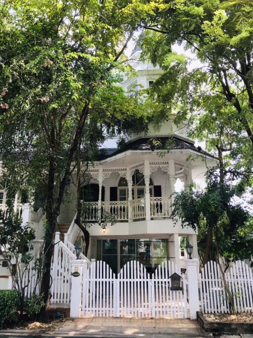 Front view of a house with a white picket fence and lush trees