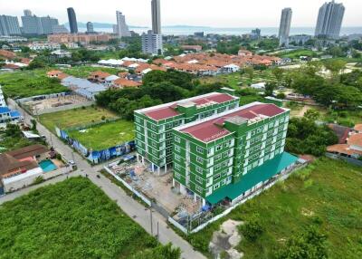 Aerial view of a green multi-story apartment building surrounded by greenery with cityscape and waterfront in the background