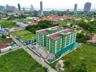 Aerial view of a green multi-story apartment building surrounded by greenery with cityscape and waterfront in the background