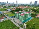 Aerial view of a green multi-story apartment building surrounded by greenery with cityscape and waterfront in the background