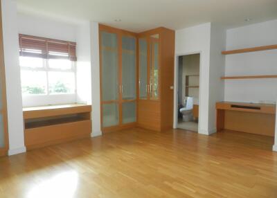 Spacious living room with wooden flooring, large window, and built-in wooden cabinets and shelves