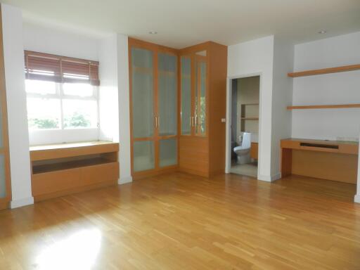 Spacious living room with wooden flooring, large window, and built-in wooden cabinets and shelves