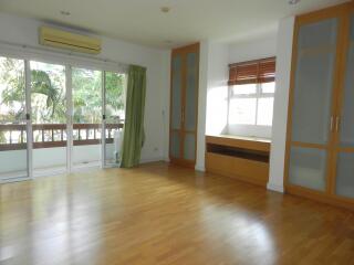 Spacious living room with wooden flooring, large windows, and balcony access