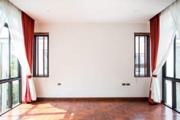 Bright living room with large windows, wooden flooring, and red curtains