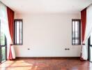 Bright living room with large windows, wooden flooring, and red curtains