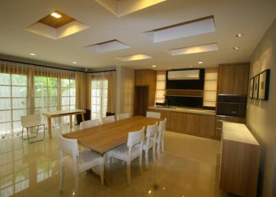 Modern dining room with large wooden table and chairs, adjacent to kitchen area with ample natural light