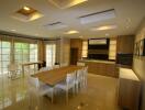 Modern dining room with large wooden table and chairs, adjacent to kitchen area with ample natural light