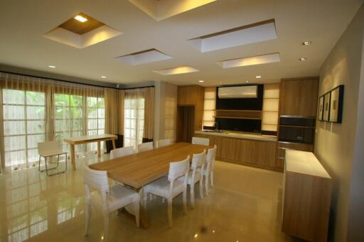 Modern dining room with large wooden table and chairs, adjacent to kitchen area with ample natural light