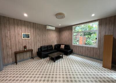 Spacious living room with wooden wall panels, black sofa set, coffee table, and large window