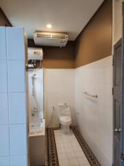 Modern bathroom with white tiles, a shower area, a toilet, and an air conditioning unit