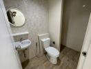 A modern bathroom with tiled walls and floor, featuring a toilet, a round mirror, and a sink