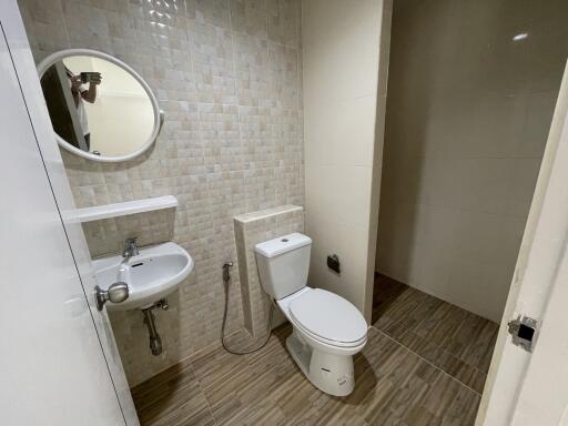 A modern bathroom with tiled walls and floor, featuring a toilet, a round mirror, and a sink