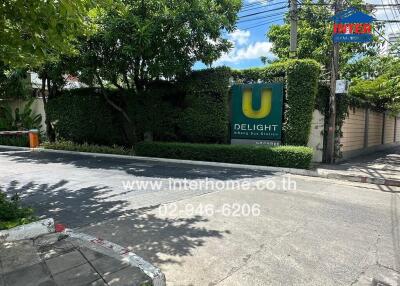 Entrance of Delight Bangkok apartment building with green hedges and sign