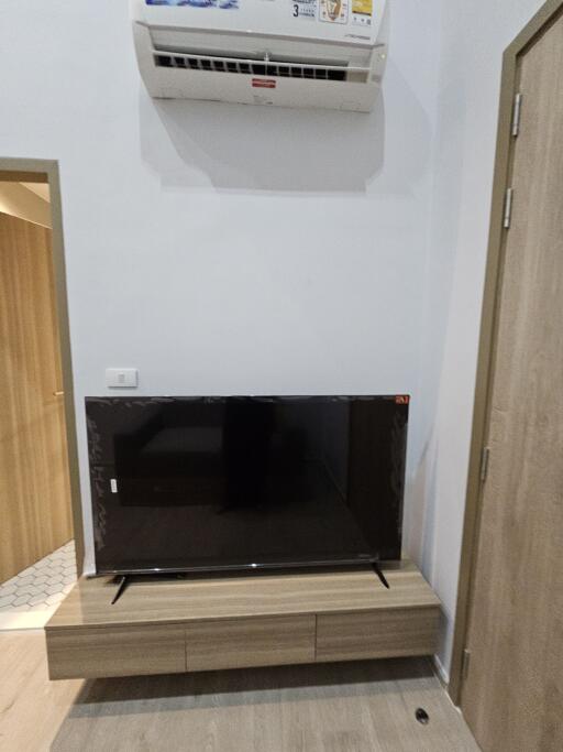 Living area with wall-mounted air conditioner and flat-screen TV on a wooden stand